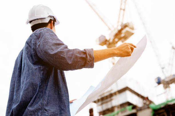 Man engineer turn around helmet holding the blueprint for check and thinking of ways and ideas for building new buildings. stock photo