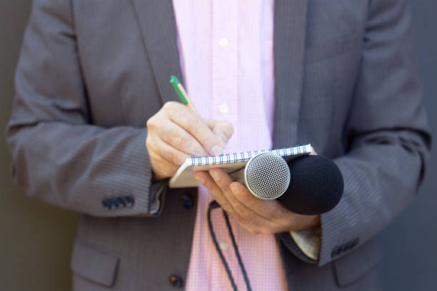 istock Journalist at news conference or media event, holding microphone, writing notes. Journalism concept. 1278402234