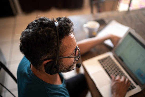 ausgereifter mann, der von zu hause aus arbeitet und headset während eines videoanrufs oder eines kundenanrufs verwendet - working at home headset telecommuting computer stock-fotos und bilder