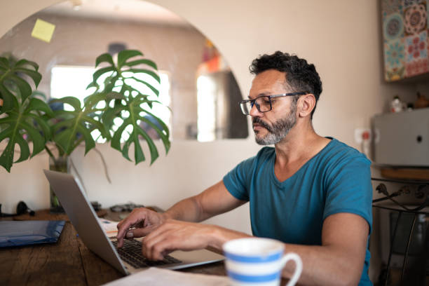 homme mûr utilisant l’ordinateur portatif pour travailler à la maison - mature men photos et images de collection