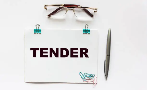 Photo of Tender, word on notepad. Glasses, pen and paper clips on a white background.
