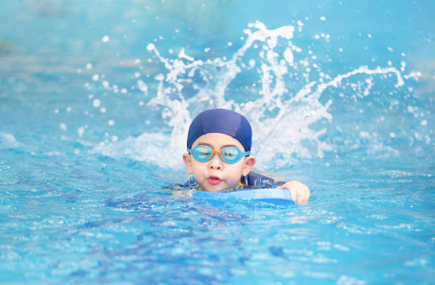 asien niedlichen jungen trägt badeanzug und schutzbrille verwendet schaum, um schwimmen im schwimmbad zu üben. gesundes kind genießt aktiven lebensstil. erfrischend und entspannen, um im sommerurlaub sportzutrainieren - color image season people wet stock-fotos und bilder