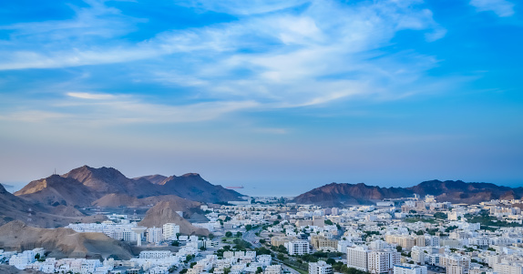 Wide View of Muscat Cityscape with blue sky and mountains from the top of a hill. From Oman.