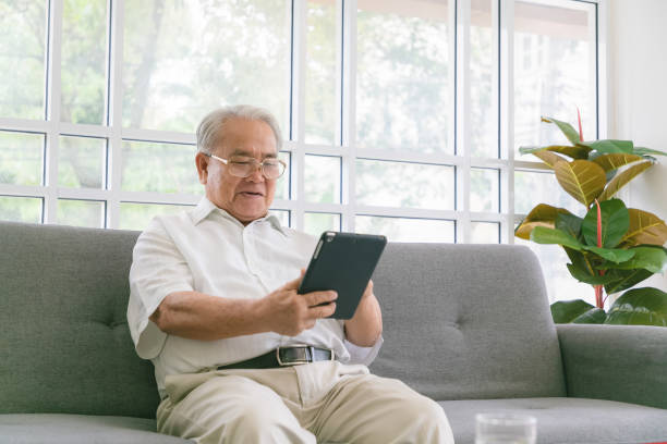 istock Senior asian man sitting on sofa and reading new on his tablet computer. 1278418288