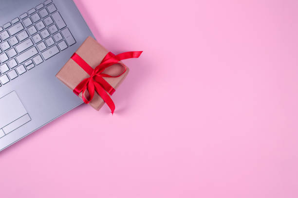 Top view on laptop computer with present box bounded with red tape on pastel pink background with copyspace for your text. Seasonal sale, black friday and cyber monday concept. Online shopping