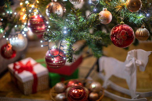 Detail of Christmas tree beautifully decorated and illuminated. Under the tree are wrapped gift boxes and more decoration.