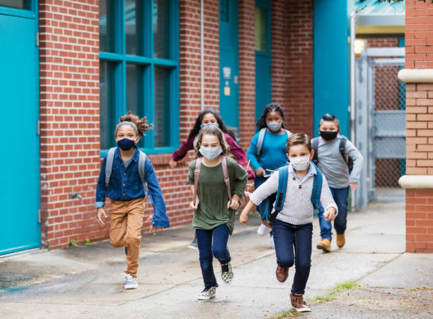 enfants d’école avec des masques de visage courant à l’extérieur du bâtiment - école photos et images de collection