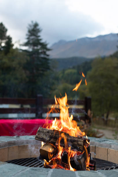 brennendes lagerfeuer in einer feuerstelle im abendlicht und bergblick - fire pit fire camping burning stock-fotos und bilder