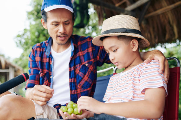 Asian father and son eating grapes when having break after fishing together