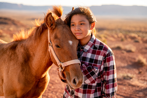 Doce años de edad Navajo chica que se posa con amor con su caballo mascota fuera cerca del Parque Tribal Monument Valley en el norte de Arizona al atardecer photo