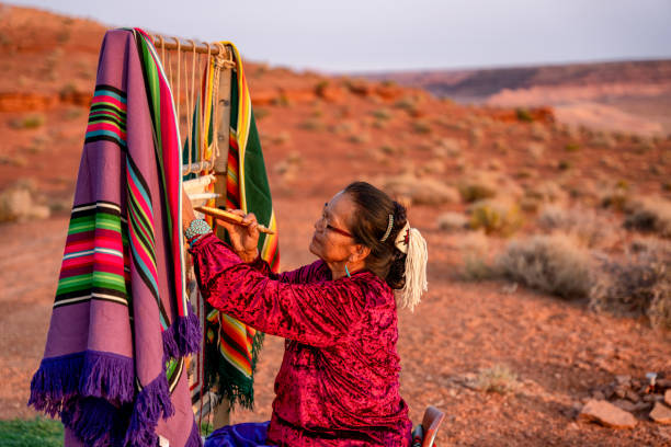 ältere navajo frau weben eine traditionelle decke oder teppich auf einem authentischen native american loom in der wüste bei dämmerung in der nähe des monument valley tribal park in nord-arizona - navajo national monument stock-fotos und bilder