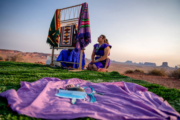 abuela navajo enseñando a su nieta cómo tejer una manta tradicional en un telar en el desierto en el parque tribal del valle del monumento al norte de arizona al atardecer - navajo national monument fotografías e imágenes de stock