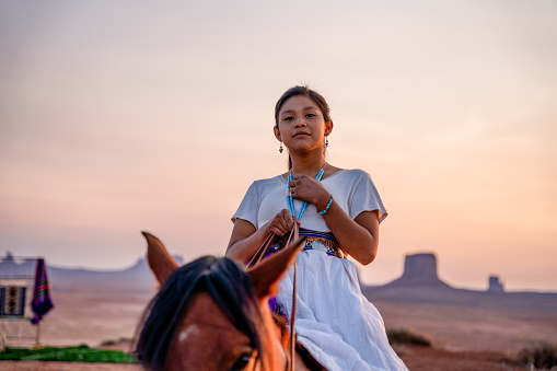 Retrato de una hermosa joven de doce años de edad Navajo niña en ropa tradicional nativa americana posando en el desierto cerca del Parque Tribal Monument Valley en el norte de Arizona al atardecer o al amanecer photo