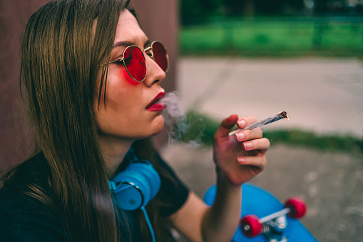 Young skateboarder woman smoking smoking marijuana joint outdoors