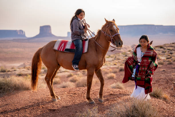 navajo children, fratello e sorella, ragazzo a cavallo a cavallo nudo con ragazza che cammina lungo il fianco nel vasto deserto nella riserva navajo e monument valley tribal park nell'arizona settentrionale - navajo national monument foto e immagini stock