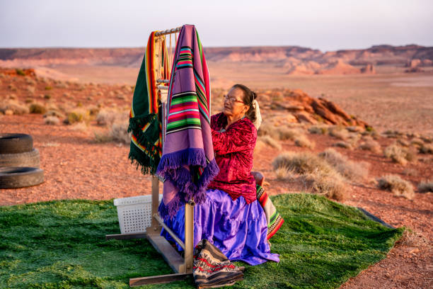 mulher navajo idosa tecendo um cobertor tradicional ou tapete em um autêntico tear nativo-americano no deserto ao anoitecer perto do monument valley tribal park no norte do arizona - national park tribal - fotografias e filmes do acervo