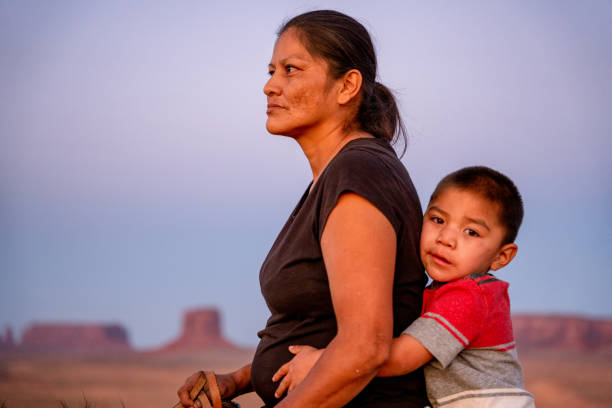 navajo mutter und junger vierjähriger sohn posieren zu pferd vor den buttes im monument valley tribal park im norden arizonas bei sonnenuntergang - navajo national monument stock-fotos und bilder