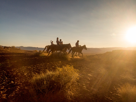 Grupo de jóvenes hermanos navajos cabalgando sus caballos desnudos a través del vasto desierto en el norte de Arizona cerca del parque tribal Monument Valley en la reserva india Navajo al atardecer photo