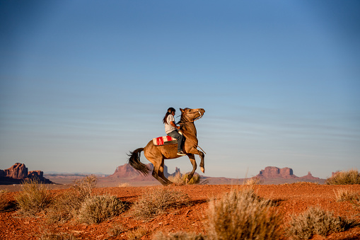Joven Navajo Teenage Boy Expertamente montando su caballo haciéndolo Buck en el desierto en la Reserva Navajo del Norte de Arizona en Monument Valley Tribal Park photo