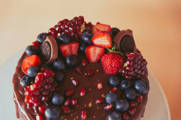 istock Appetizing chocolate cake decorated with strawberries, blueberries and a pomegranate on an orange background. 1278443070