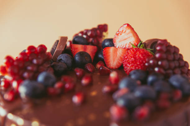 istock Appetizing chocolate cake decorated with strawberries, blueberries and a pomegranate on an orange background 1278443118