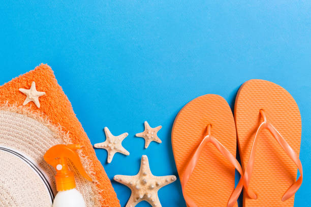 istock Summer beach flat lay accessories. Sunscreen bottle cream, straw hat, flip flops, towel and seashells on colored Background. Travel holiday concept with copy space 1278444629