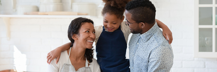 Horizontal photo banner of happy young african american biracial couple parents holding small adorable kid girl on hands, enjoying spending weekend leisure time in kitchen, website header design