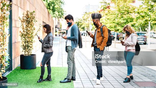 Young People Waiting In Line Practising Social Distancing At City Shop New Normal Lifestyle Concept With People Wearing Face Mask On Urban Queue Bright Backlight Filter Stock Photo - Download Image Now