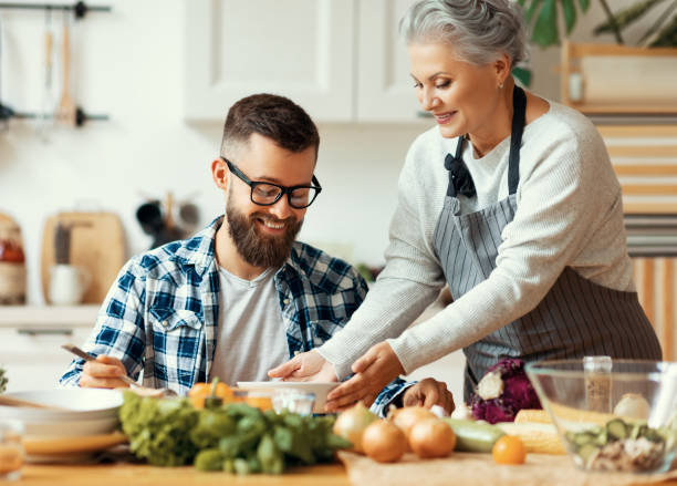 happy mother serving healthy food to adult son at home - family mother domestic life food imagens e fotografias de stock