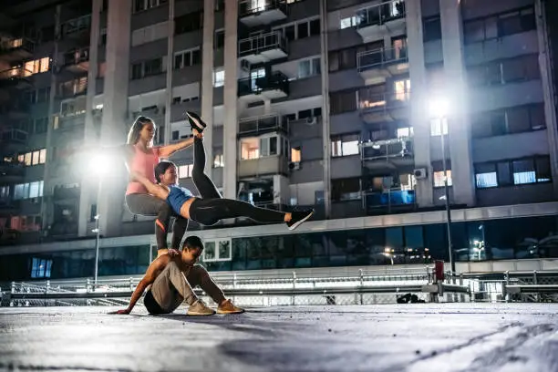 Three young Caucasian athlete people practicing acroyoga in public garage.