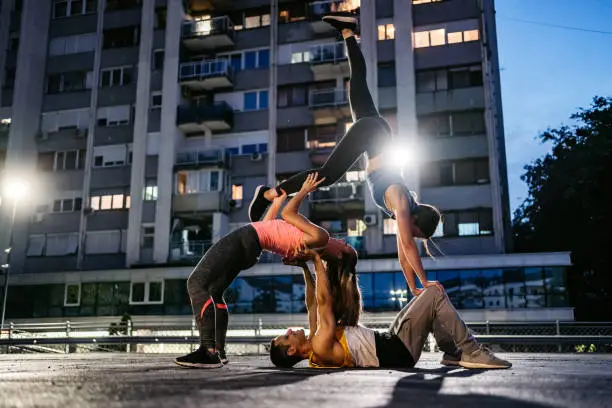 Three young Caucasian athlete people practicing acroyoga in public garage.