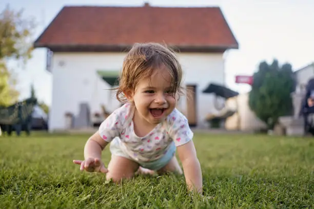 Photo of Ecstatic baby girl crawling on grass outdoors in a back yard in summer