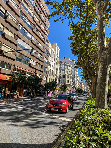 Valencia, Spain - October 3, 2020: Red car moving along Ferdinand the Catholic avenue. This is a traditional street built along the enlargement of the city off the limits of the original walled city in the 19th century