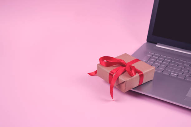 istock Front view on laptop computer and present box with red bow on pastel pink background with copyspace for your text. Seasonal sale, black friday and cyber monday concept. Online shopping 1278461536