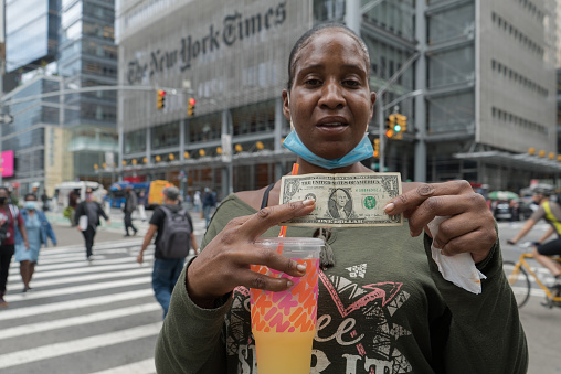 Manhattan, New York. October 01, 2020. A homeless woman poses with a dollar bill in her hands in front on the New York Times building in midtown.