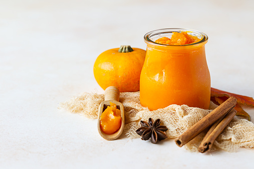 Canned organic pumpkin puree in glass jar with fresh pumpkin, cinnamon and anise on light background. Ingredient for Thanksgiving, autumn or winter recipes.