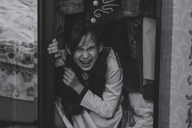 Mad scary girl in cupboard at dark night. Horror background with child possessed by devil. Demon possessed little girl in closet at night. Ghost of little girl at dark night. Child ghost in cupboard.