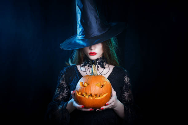 Mysterious Halloween sexy witch holding carved pumpkin on black background. stock photo