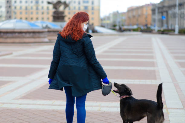 istock Young female using a face mask as a coronavirus spreading prevention walking with her dog. Global COVID-19 pandemic concept image. 1278469984
