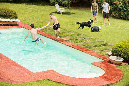 Shot of two men jumping into a swimming pool at holiday resort