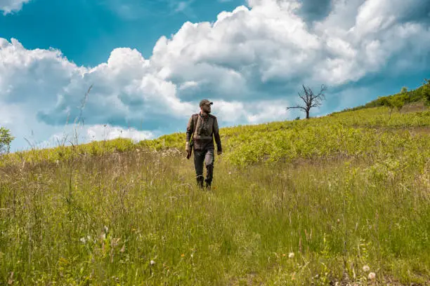 Photo of Hunter climbing a hill in search for prey with beautiful cloudscape behind him