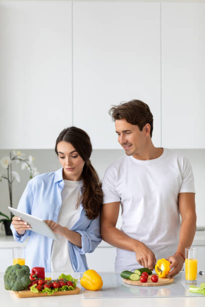 istock Happy millennial couple stand in modern kitchen cooking salad, man chopping vegetables while his girlfriend is using a digital tablet looking for a recipe. 1278472621
