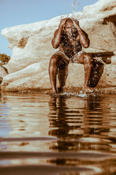 istock Male sitting on rock splashing his body 1278476097
