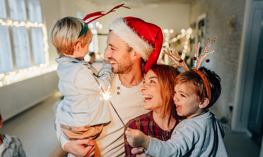 Photo of a cheerful family with two small children, celebrating Christmas at home