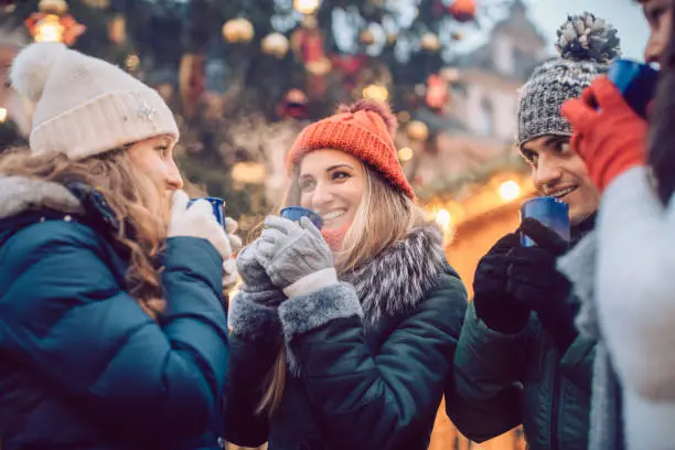 Group of friends drinking mulled wine in the cold on a Christmas Market with fun and laughter