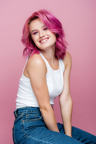 young woman with colorful hair smiling isolated on pink
