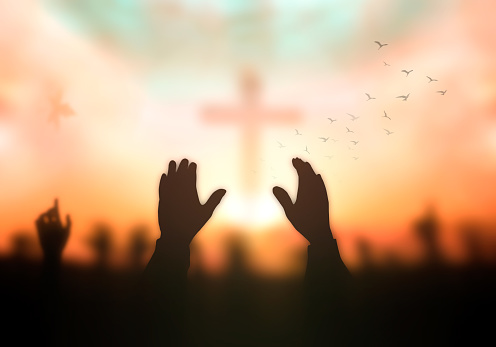 Silhouette christian hand rising over blurred cross on spiritual light background