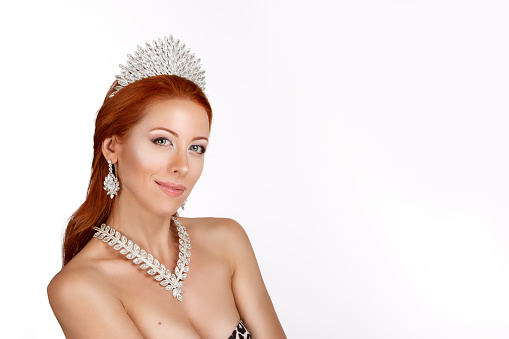 Beauty queen. Woman with crown on head and diamond necklace on her neck with positive facial expression looking at you camera posing isolated white background. Multicultural Caucasian Irish model