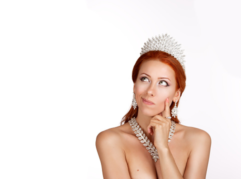 Thinking looking on copy space. Portrait pensive thoughtful skeptical face expression woman with diamond crown and necklace, thinking finger hand on cheek looking up at copy space on white background