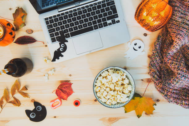 Top view Halloween Movie party concept. Flat lay composition with laptop, popcorn bowl, decorative pumpkin, bats, ghost silhouettes, sweets, fall leaves, warm plaid on wooden background. Cozy holiday concepto de fiesta de halloween de la película de halloween de la vista superior. composición plana con portátil, cuenco de palomitas de maíz, calabaza decorativa, murciélagos, siluetas fantasma, dulces, hojas de otoño, cálido a cuadros sobre fondo